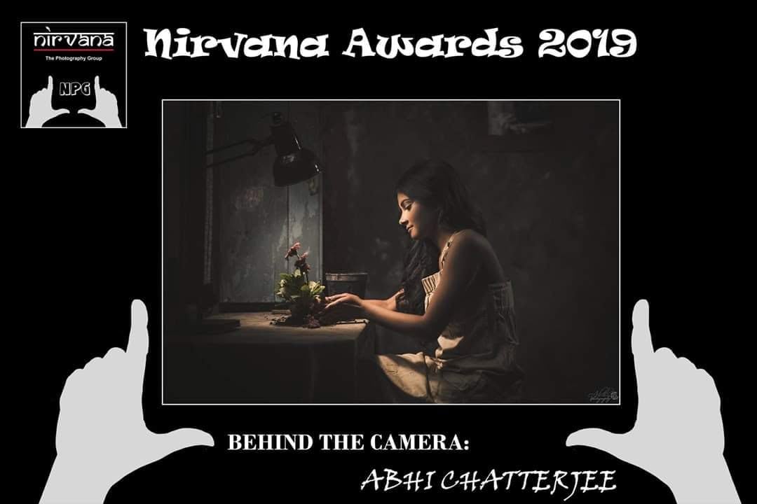 A Nirvana Awards 2019 card holding up a framed picture of a woman at a table with a lamp.