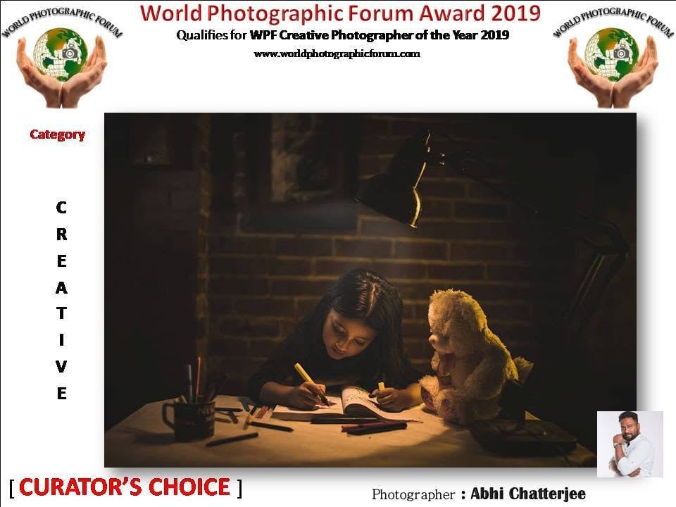 A World Photographic Forum poster marked Curator's Choice, showing a girl writing beside a teddy bear.